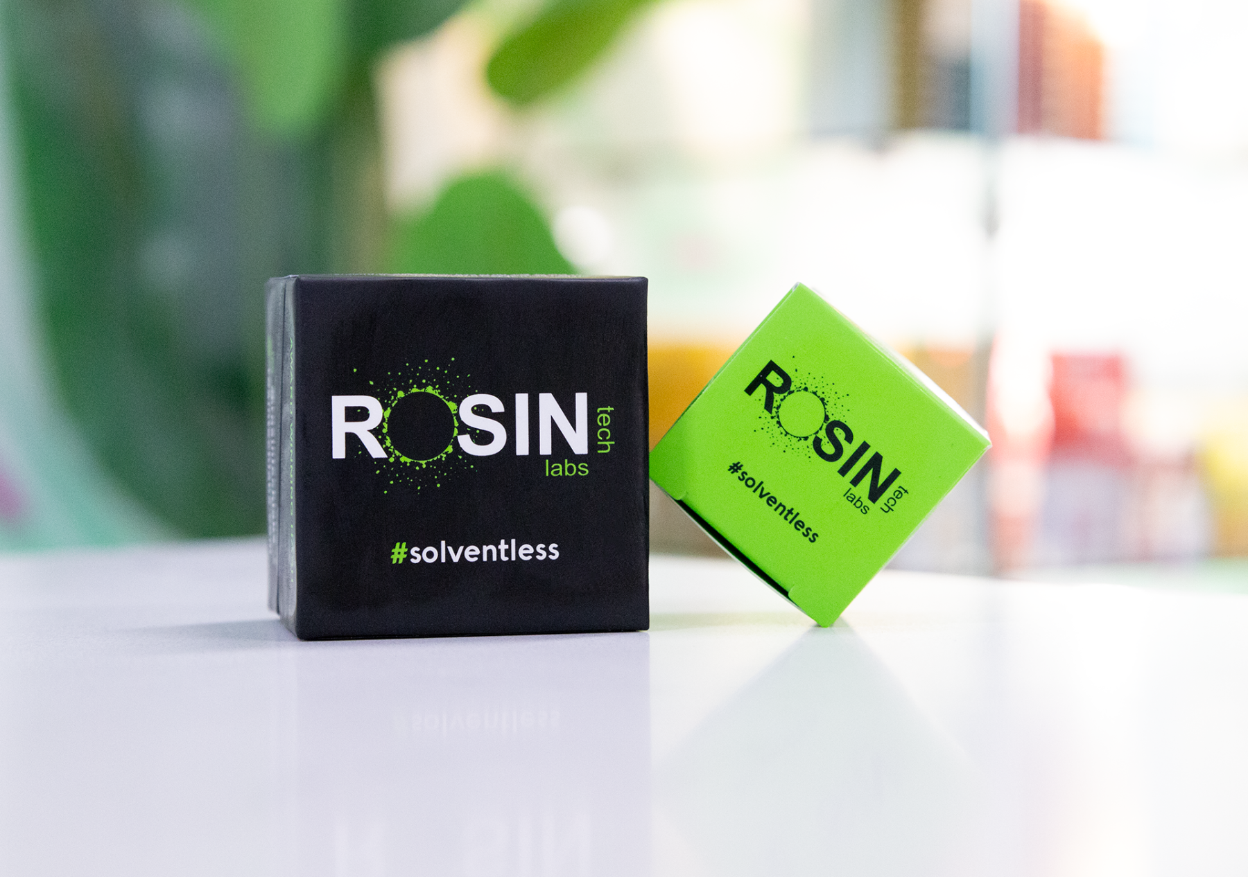 Rosin Tech Labs solventless cannabis concentrate packaging, featuring a black box and a neon green box with the #solventless label, displayed on a white surface with a blurred background.